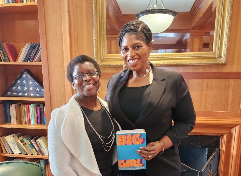 Two people pose in a library. One is holding a book.