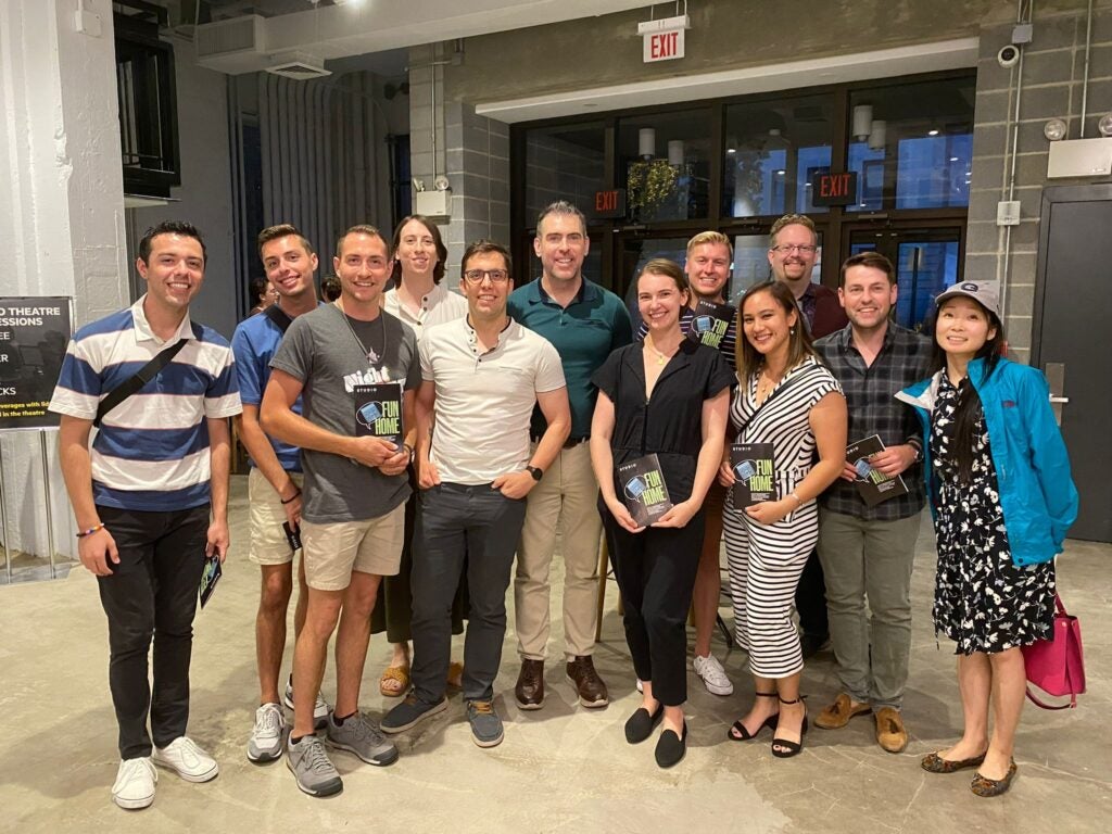 A large mixed group of people stand together to pose for a photo inside a theater entrance.